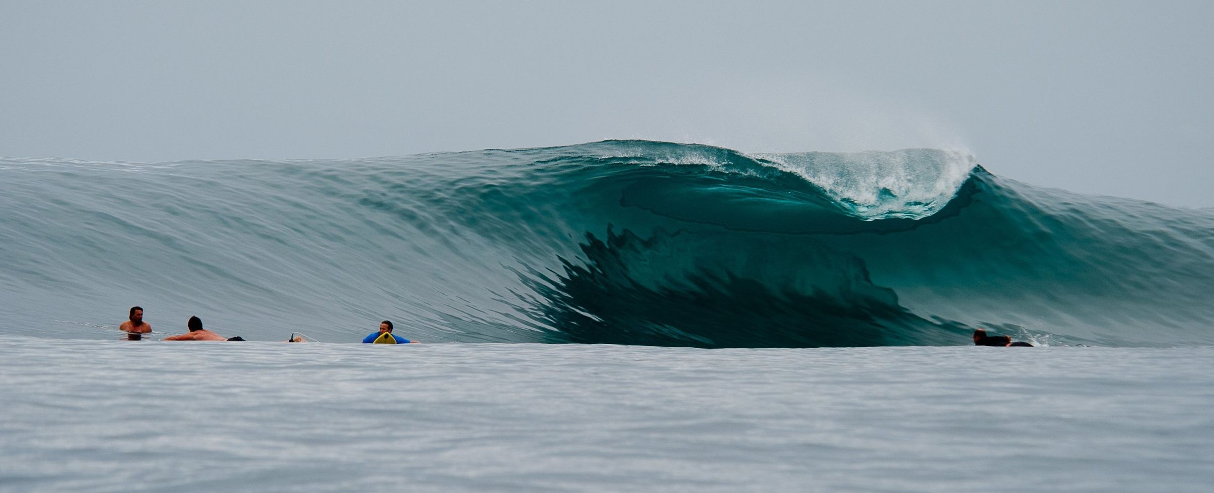 A glassy left barrelling over a reef with surfers waiting on the shoulder
